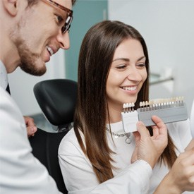 Smiling dentist helping patient pick veneer shade